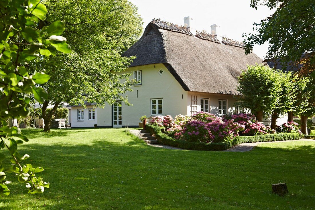 Well-tended lawn and flowerbeds in garden of restored country house with thatched roof