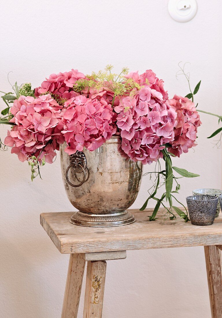 Pink hydrangea flowers in silver vessel on rustic wooden stool