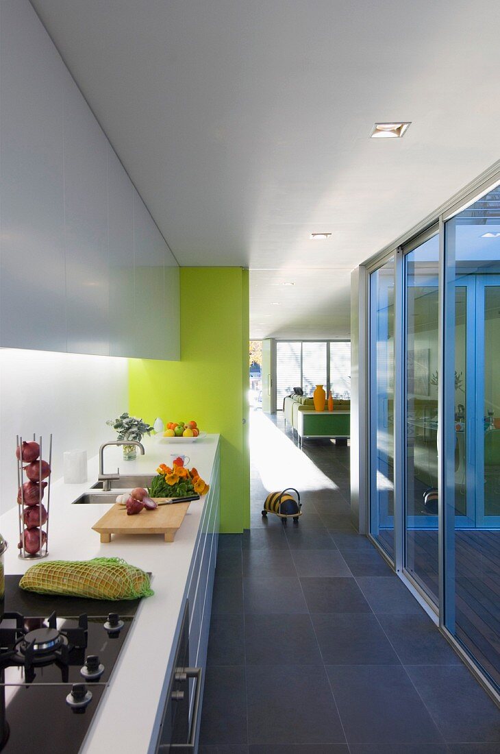 Durchgang mit weisser Küchenzeile und Glasfront zur Holzterrasse; ein pastellblauer Türrahmen und eine gelbe Wandfläche sorgen für Fröhlichkeit