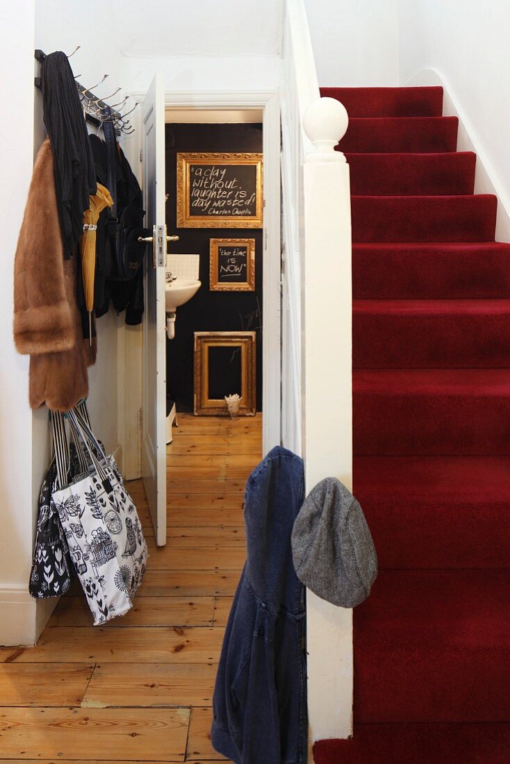 Treppe mit rotem Teppichbelag in traditionellem Treppenhaus mit offener Badtür und Blick auf goldene Bilderrahmen