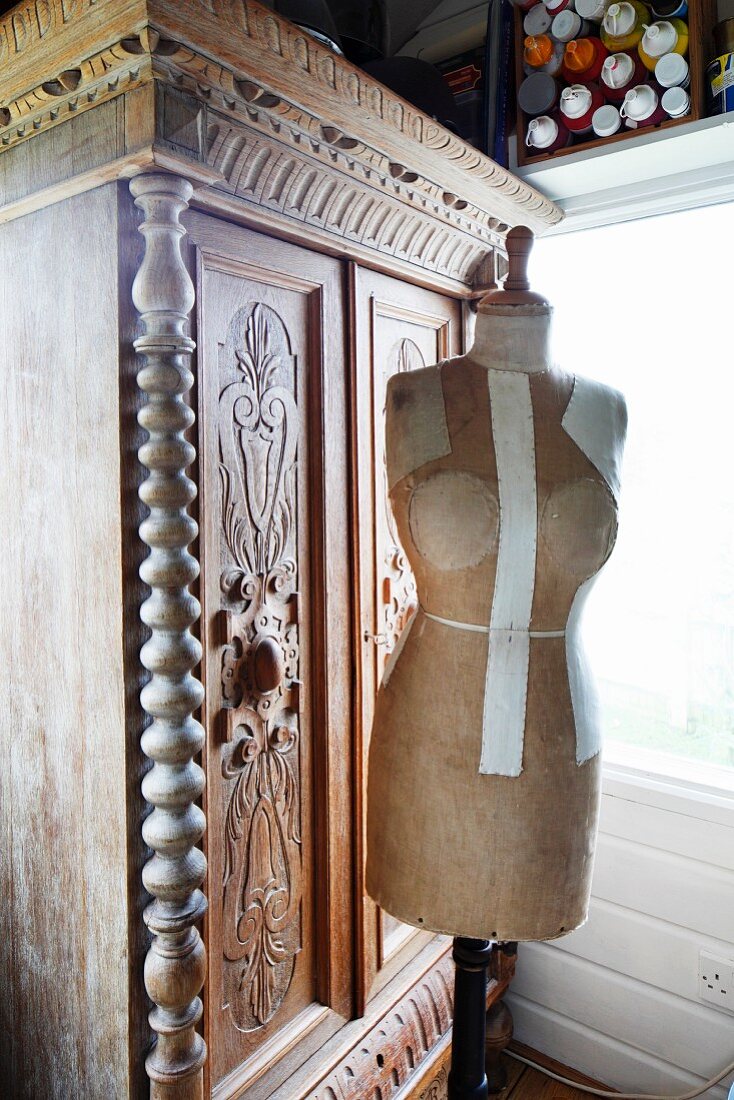 Vintage tailors' dummy in front of antique, 19th century cupboard of carved wood in corner