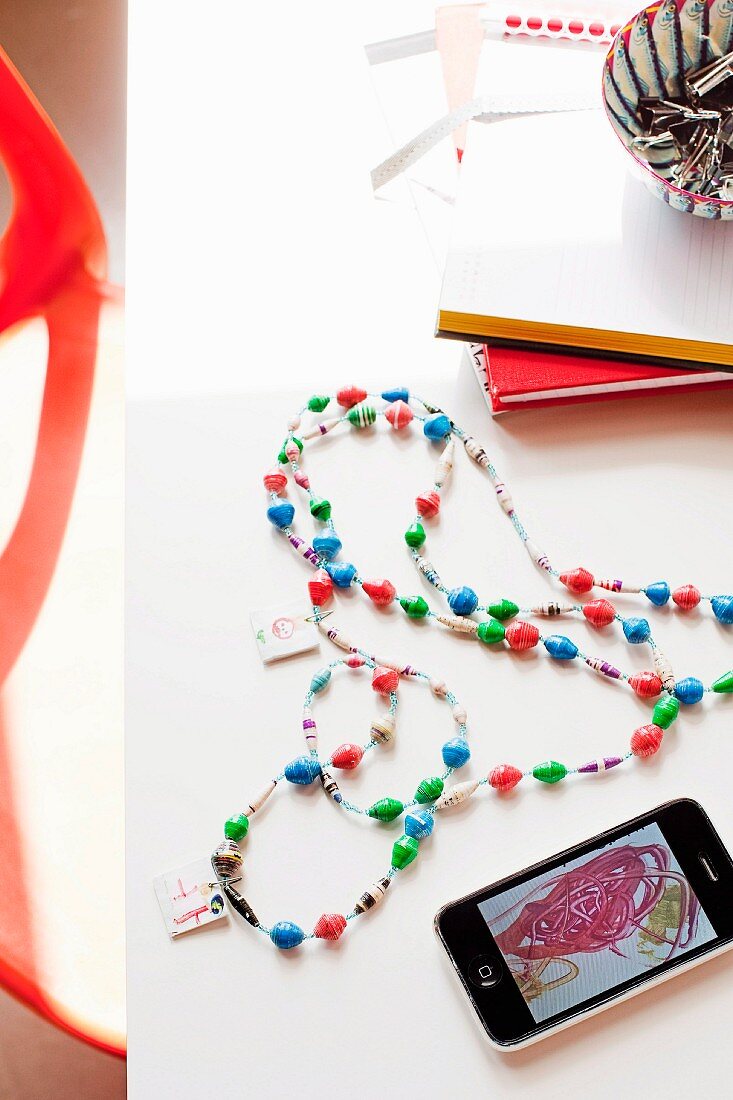 Hand-crafted necklace with painted pendants & smartphone showing photo of child's painting