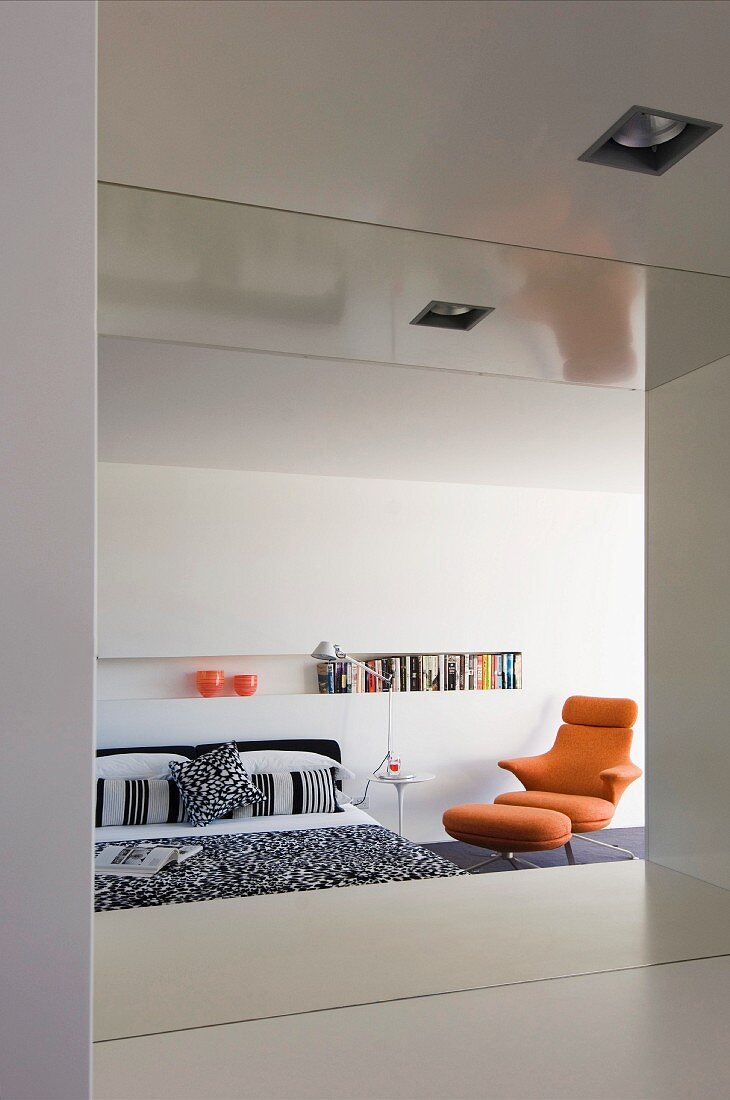 Minimalistisches Schlafzimmer mit Wandnische als Bücherregal und einem orangefarbenen Designersessel