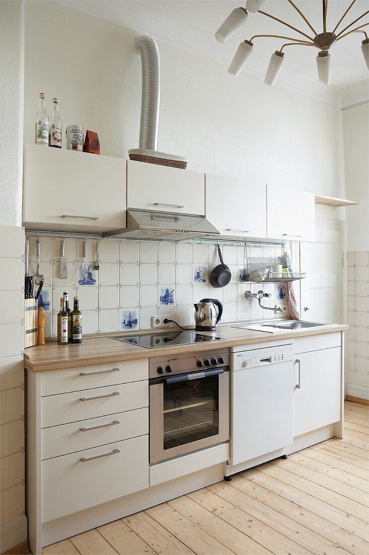 Funktionale Küche mit weissen Schrankfronten in ländlichem Ambiente und spinnenförmige Hängeleuchte im 50er Jahre Stil