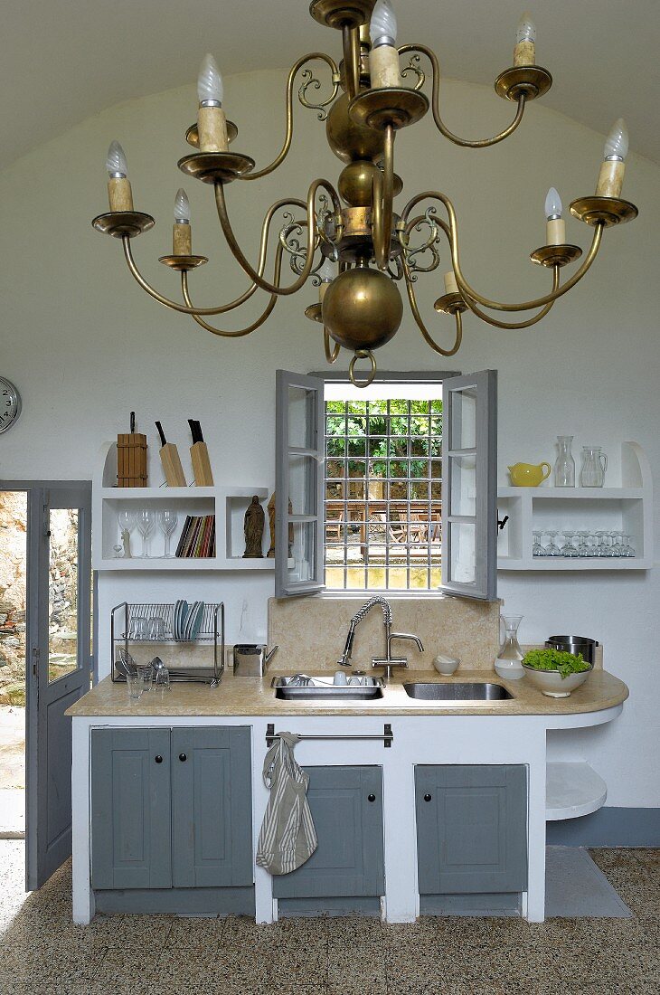 Brass chandelier in white kitchen with grey unit doors and window grille