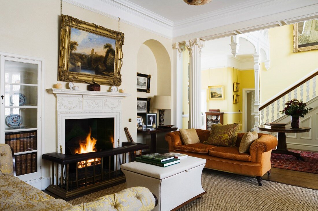 Verschiedene, traditionelle Polstermöbel vor brennendem Kaminfeuer in englischem Herrenhaus