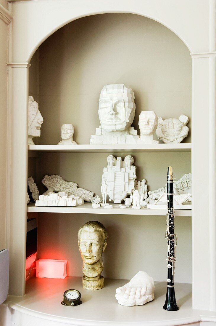Carved figurines and clarinet in old, classic fitted shelves in niche