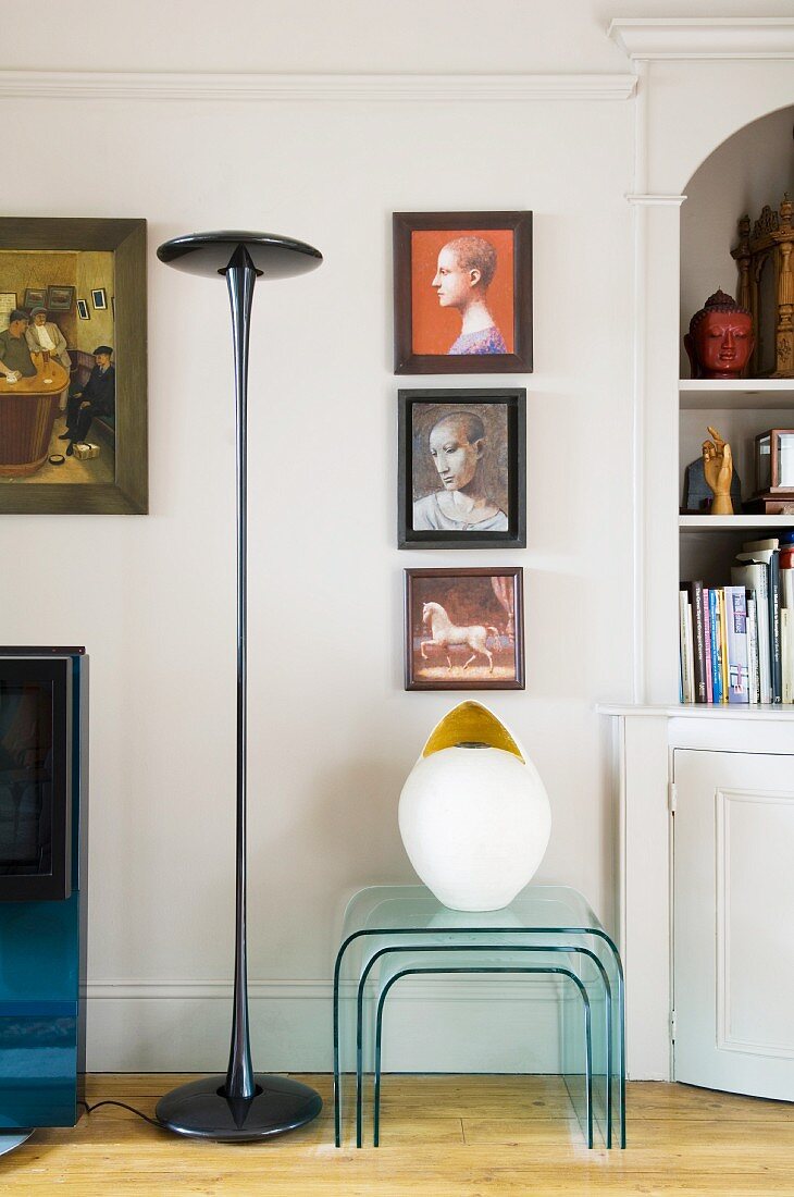 Designer standard lamp and nest of plexiglass tables below collection of paintings on wall