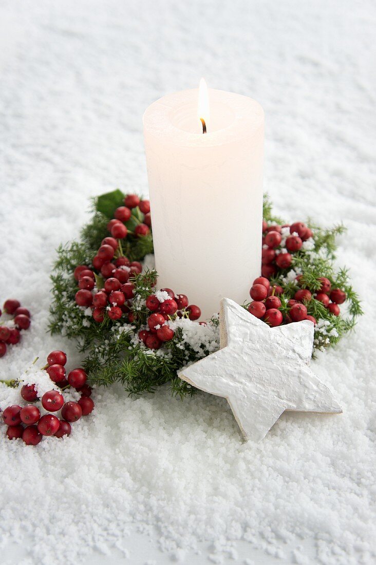 Candle with holly berries and wooden star in snow