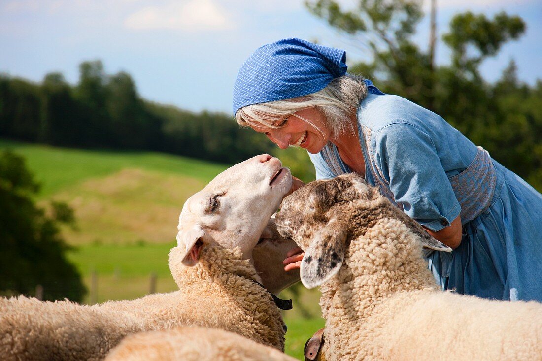 Germany, Bavaria, Mature woman playing with sheep on farm