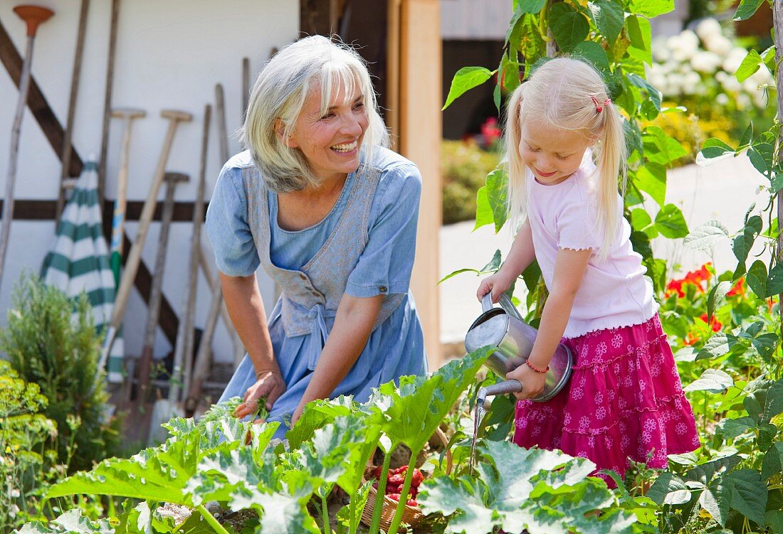 Ältere Frau und Mädchen gießen Pflanzen im Garten