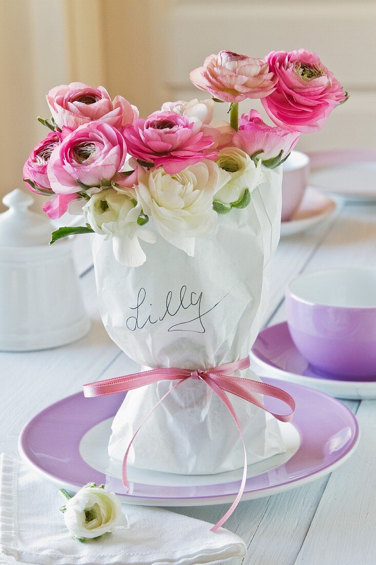 Woman's name on wrapped ranunculus bouquet with pink ribbon on plate