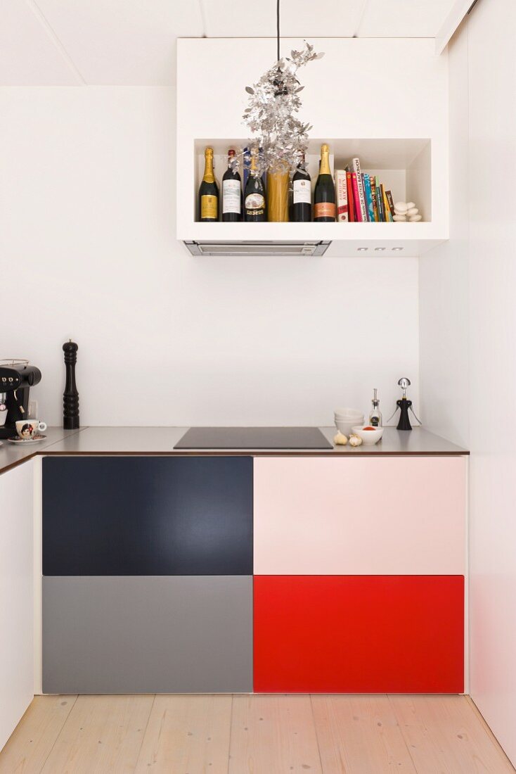 Minimalistische Küche mit farbigen Paneelen an Küchenunterschrank unter eingebautem Dunstabzug mit integriertem Regal