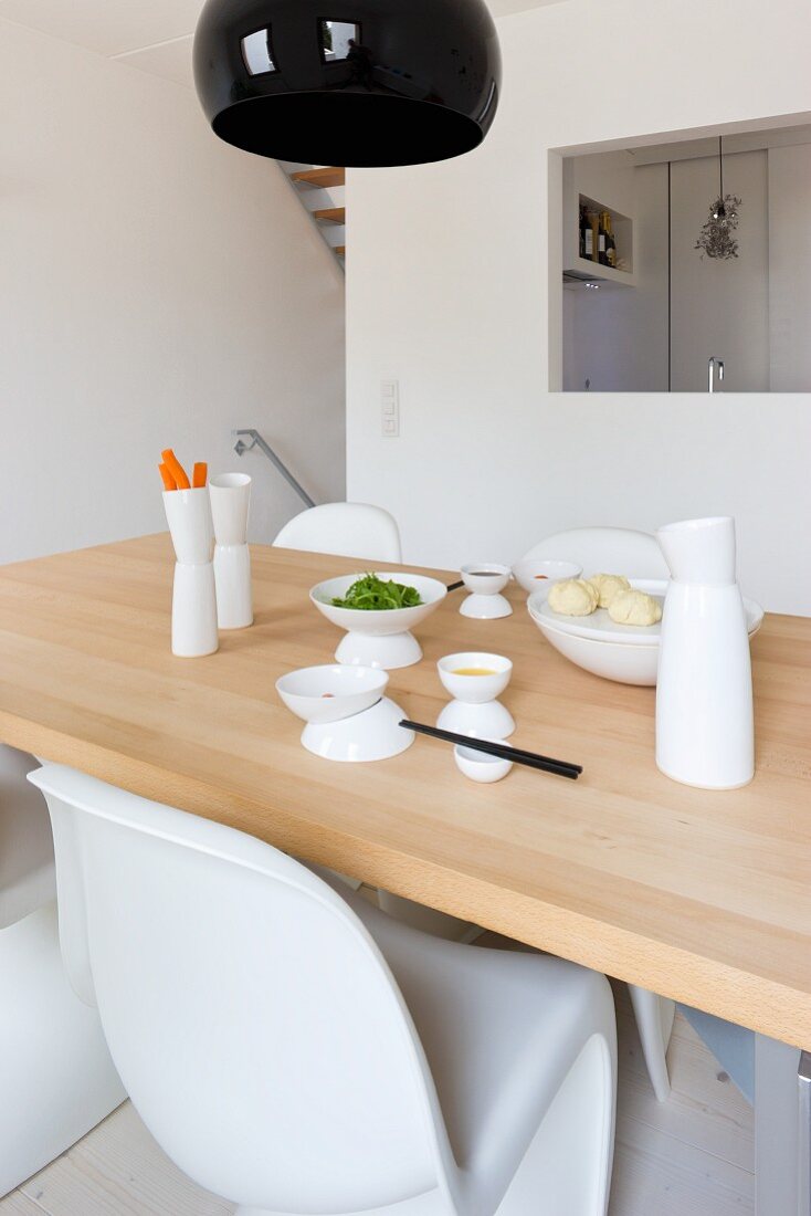 Asiatische Geschirr auf Holztisch vor Küchenwand mit Durchreiche in minimalistischem Esszimmer