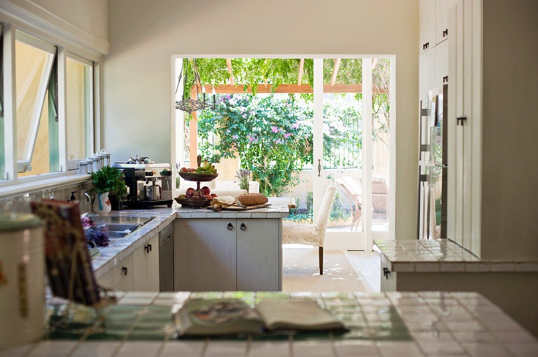 View across tiled kitchen counter into open-plan kitchen with view of garden through terrace doors