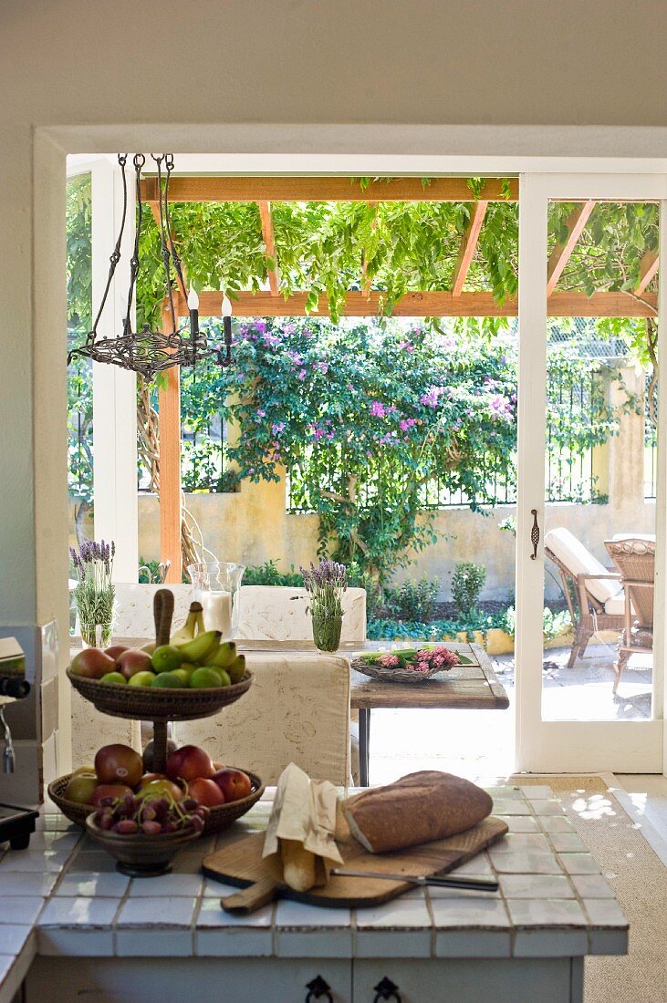 Etagere mit Obst auf gefliester Küchenzeile vor offener Terrassentür und Blick in kleinen Vorgarten