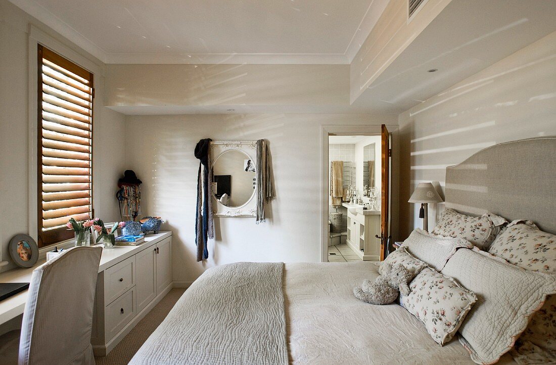 Double bed with upholstered headboard and ecru bed linen in simple bedroom with open door leading to bathroom