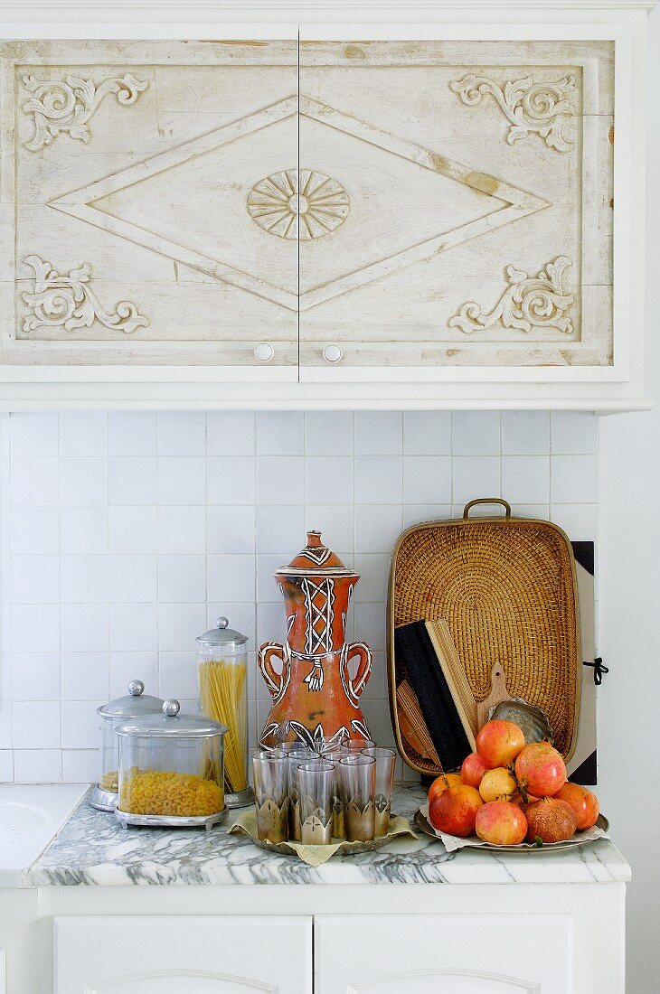 Küchenzeile mit Obstteller und marokkanischen Teegläsern auf Marmorplatte vor gefliestem Spritzschutz unter Hängeschrank mit orientalischem Muster auf Türen