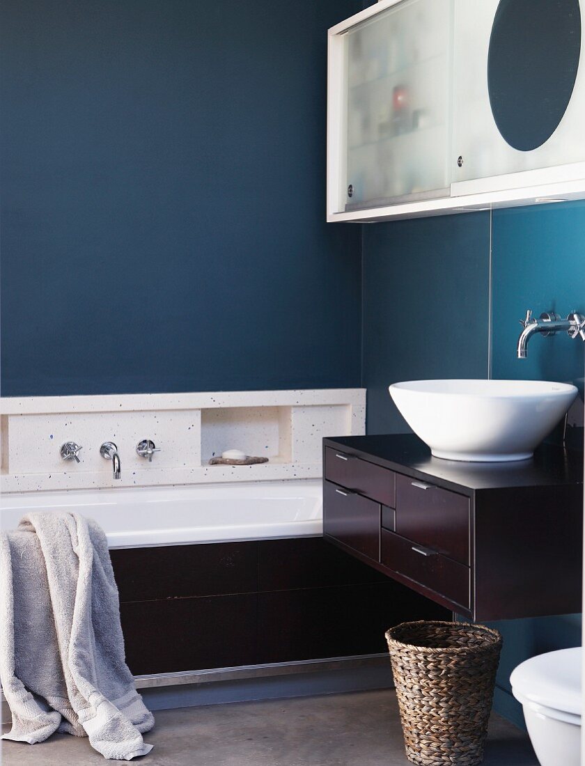 Bathtub & washstand with dark brown wood cladding in bathroom with petrol blue walls