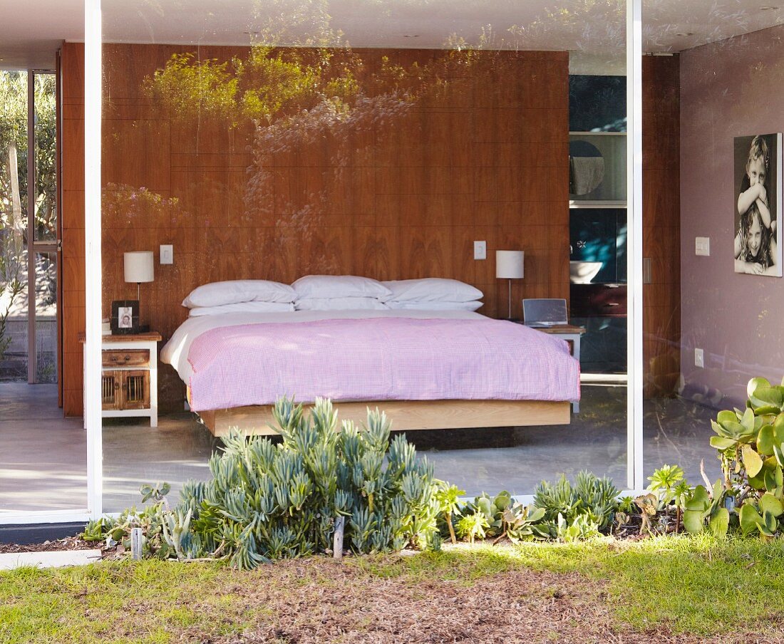 Blick auf Schlafbereich mit Beet in verglastem Wohnhaus