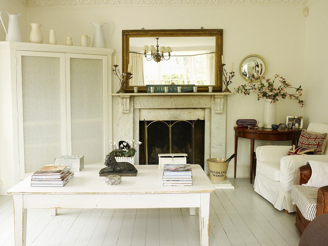 Wohnzimmer mit offenem Kamin, Wandspiegel, weiss lackiertem Tisch, Polsterstühlen, Eckschrank und antikem Beistelltisch