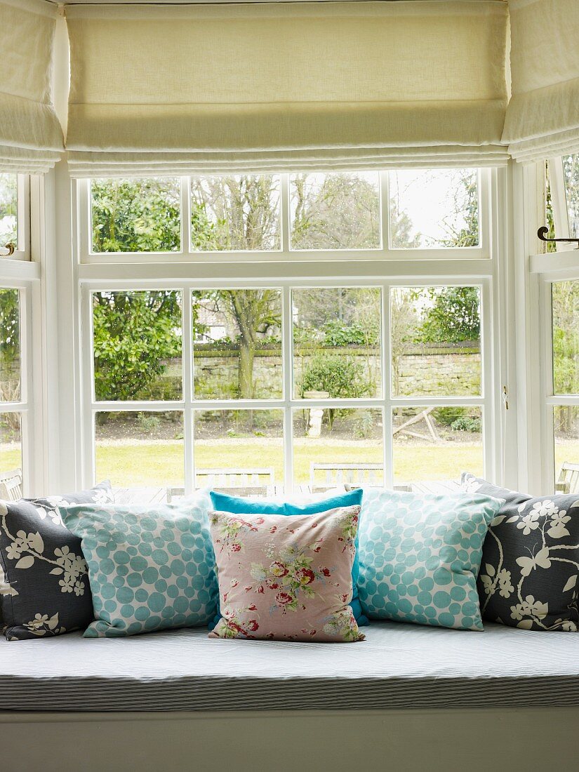 Sitzbank mit Kissen vor einem Fenster mit Gartenblick