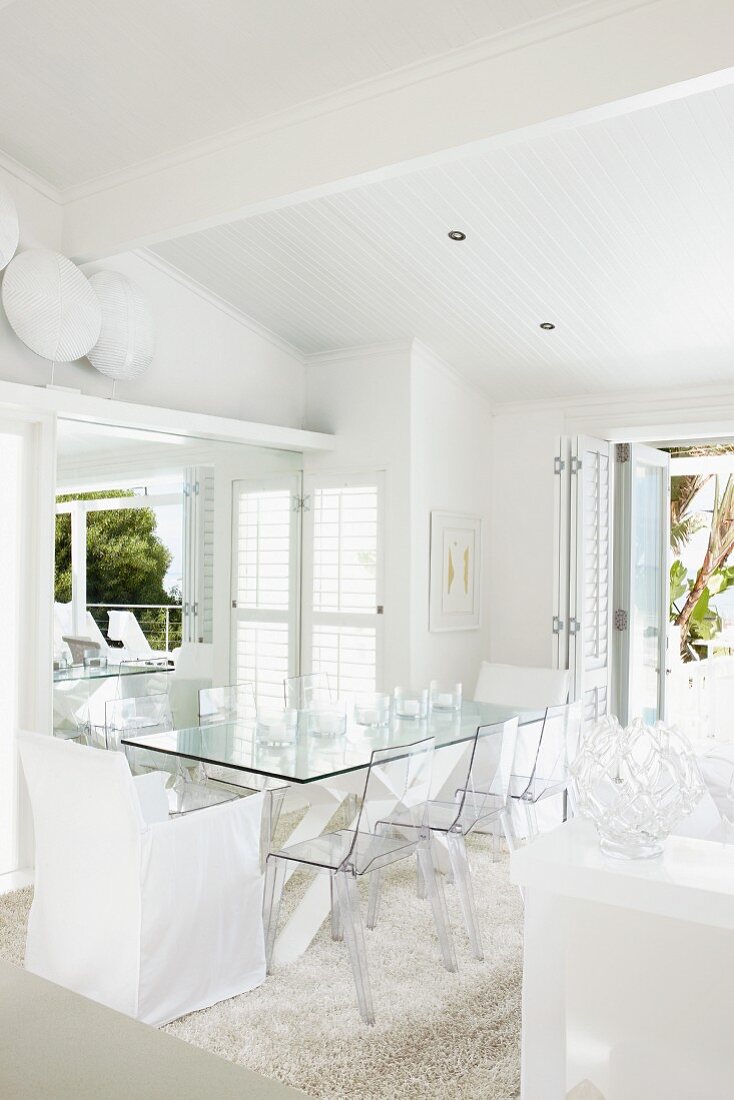 Dining area with transparent, plastic chairs and chair with white loose cover around glass table in designer interior