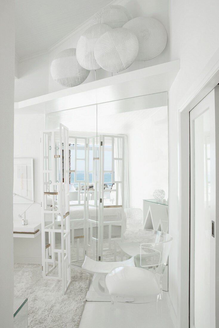 weiße Wohnzimmerecke mit Paravent-Gestell vor Spiegelschrank, darüber eine Ablage mit Schild-Sammlung