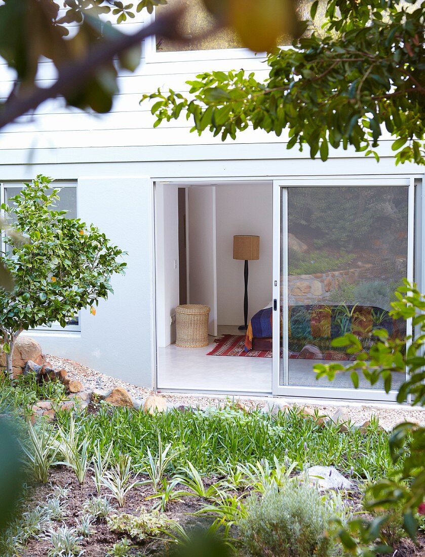 Blick über Garten durch offene Terrassen-Schiebetür auf das Schlafzimmer