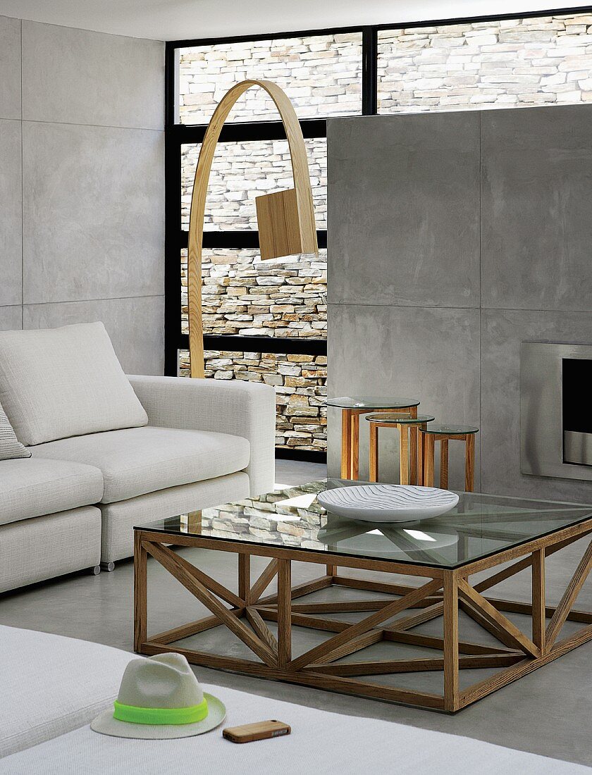 Couchtisch mit Holzgestell vor Sofa und Designer Bogenlampe aus Holz in zeitgenössischem Wohnraum mit Sichtbetonwand