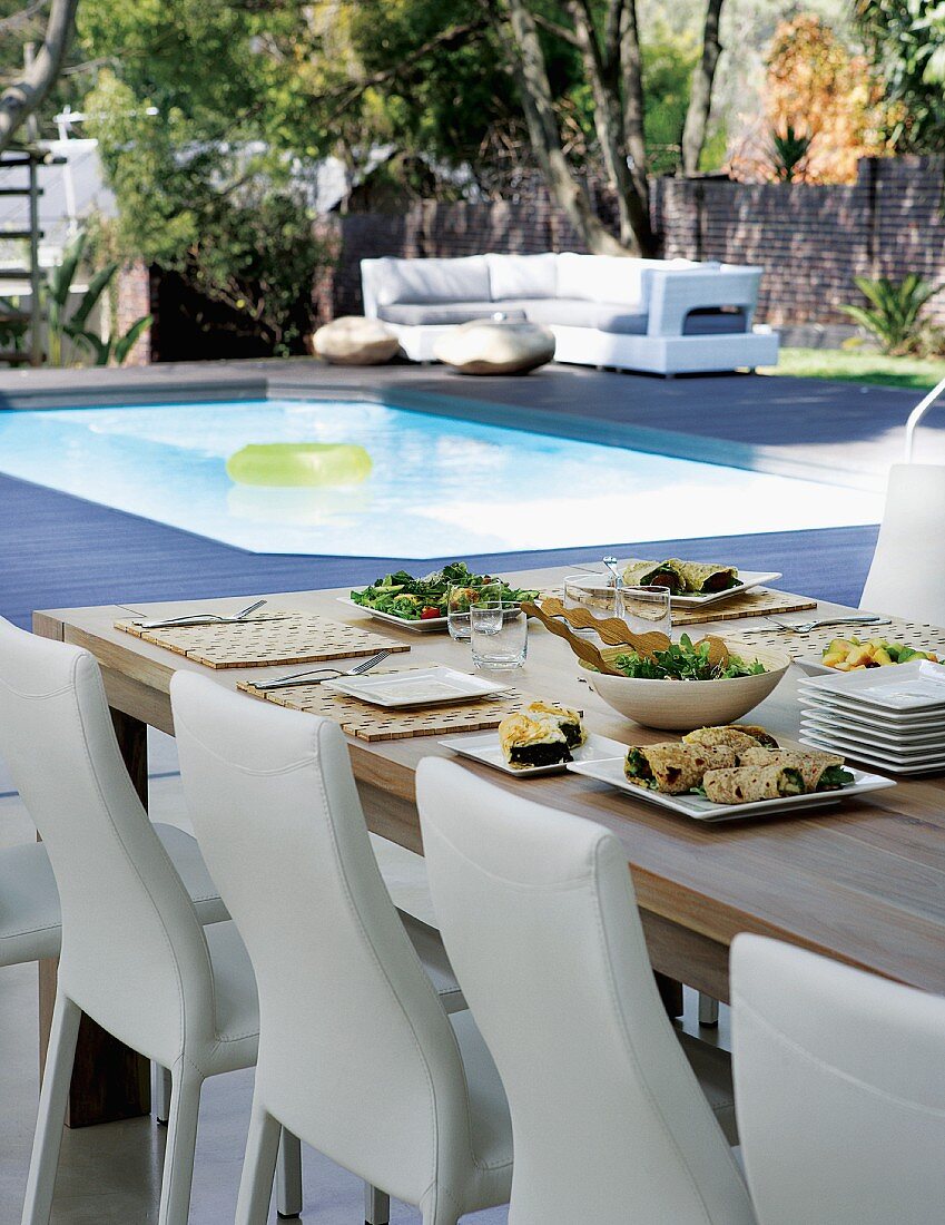weiße lederbezogene Stühle an gedecktem Tisch und Blick auf Pool im Garten