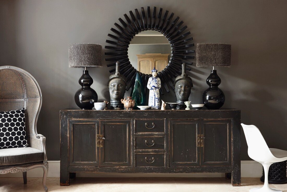 Objets d'art and table lamps with fur lampshades on shabby chic sideboard below black sunburst mirror