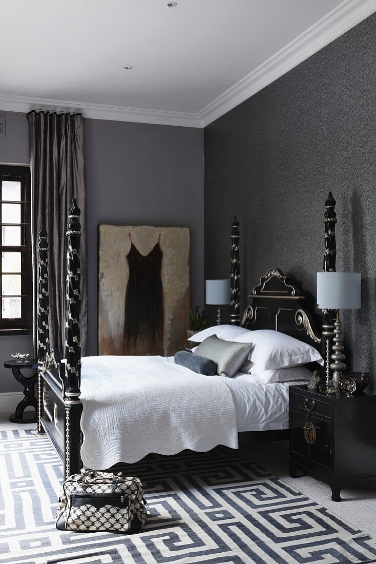 Grauer Schlafraum mit kunstvollem, chinesischen Doppelbett mit hohen silberverzierten Bettpfosten; auf dem Boden ein Webteppich mit geometrischem Muster