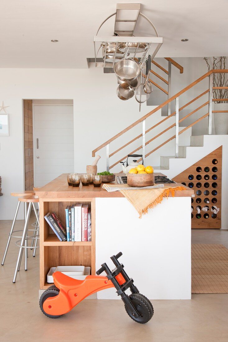 Offener Wohnraum mit Treppenaufgang, Kücheninsel und darüberhägendem Kochgeschirr aus Edelstahl
