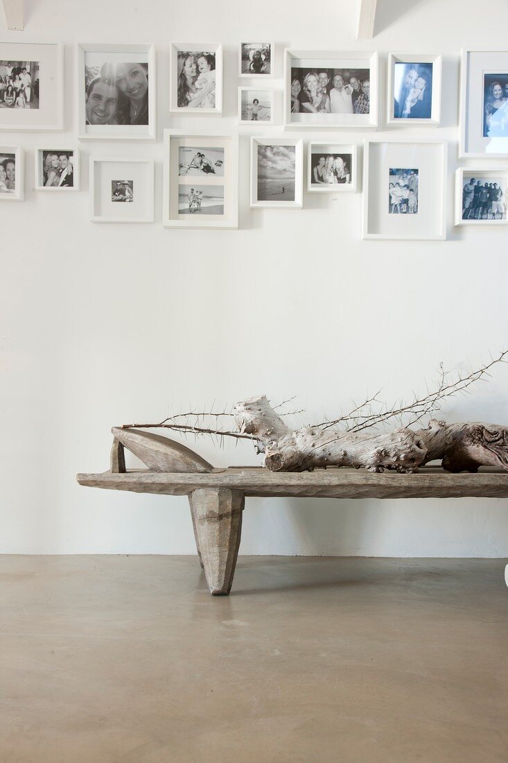 Collection of black and white photographs on white wall above driftwood lying on rustic table