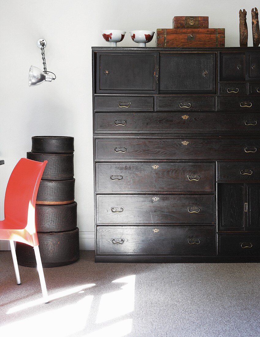 Antique, black chest of drawers next to stacked hatboxes against white wall