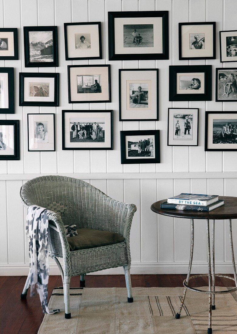Rattanstuhl an weisser Holzwand mit großer, schwarzgerahmter Fotosammlung