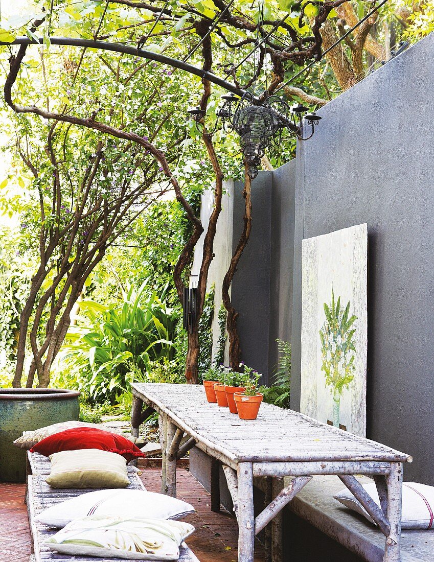 Rustic seating area with furniture made from logs against grey-painted terrace wall