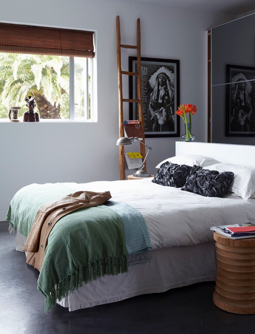 Double bed in front of mirrored sliding wardrobe doors; ethnic-style wooden objets and picture of Native American on wall