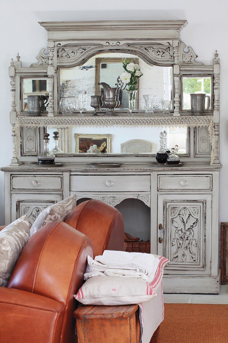 Sofa with brown, leather upholstery in front of traditional dresser painted pale grey with mirrored top against wall
