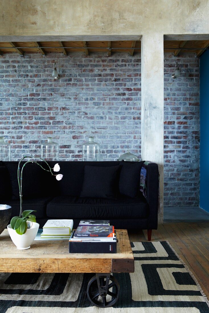 Durchgang mit Ziegelsteinwand; im Vordergrund eine schwarze Couch und ein selbstgemachter Couchtisch mit Rädern auf schwarz-weiss gemustertem Teppich