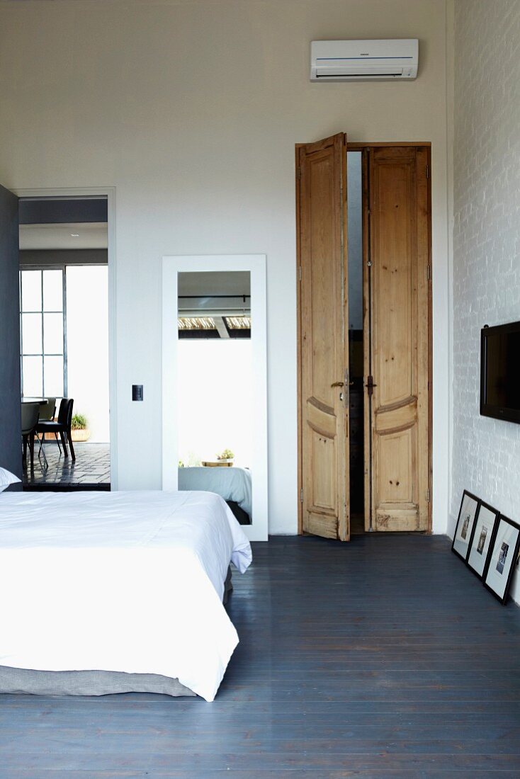 Narrow double doors in bright bedroom with blue-stained wooden floor and large, full-length mirror