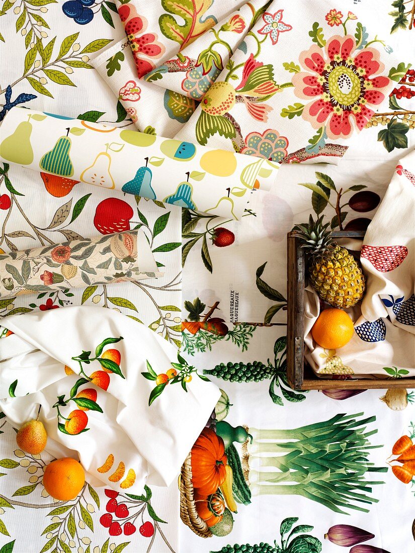 Farbenfrohe Tischwäsche und Papierrollen mit Blumen-, Obst- und Gemüsemotiven