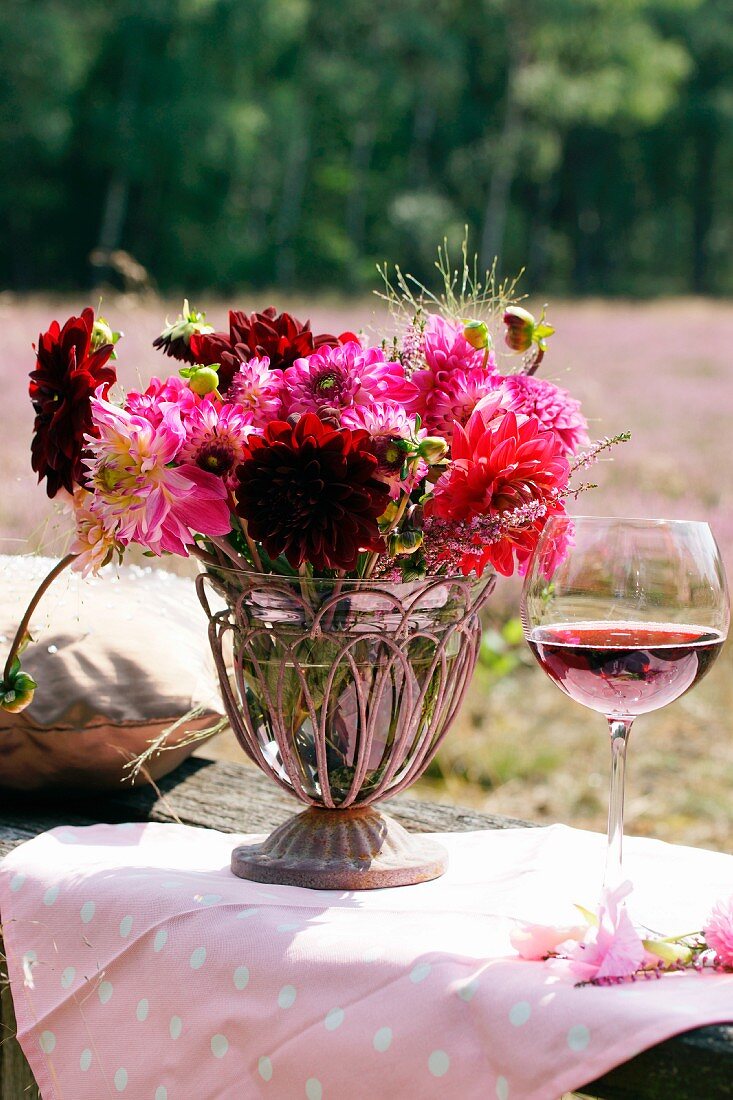 Sommerlicher Blumenstrauss mit Dahlien und Erika sowie ein Rotweinglas auf Gartentisch