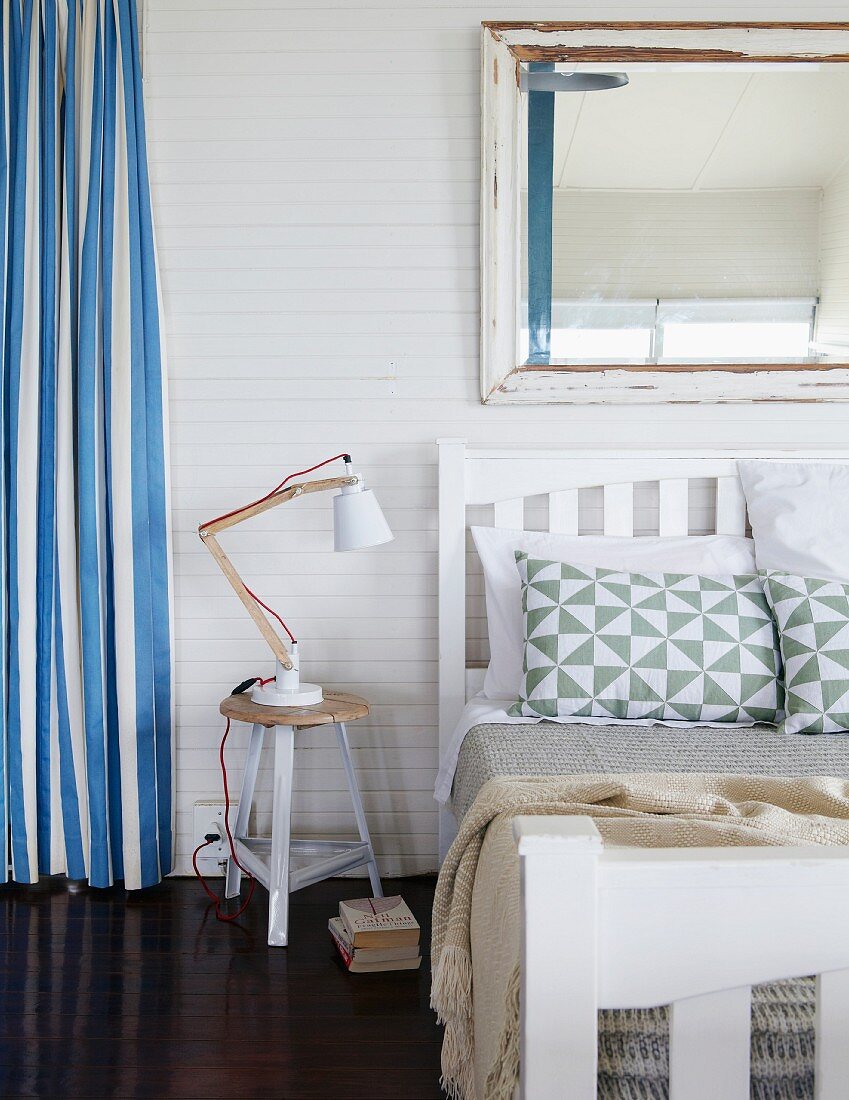 Bedroom on mezzanine with blue and white striped curtain and large, shabby-chic mirror on wall above white double bed