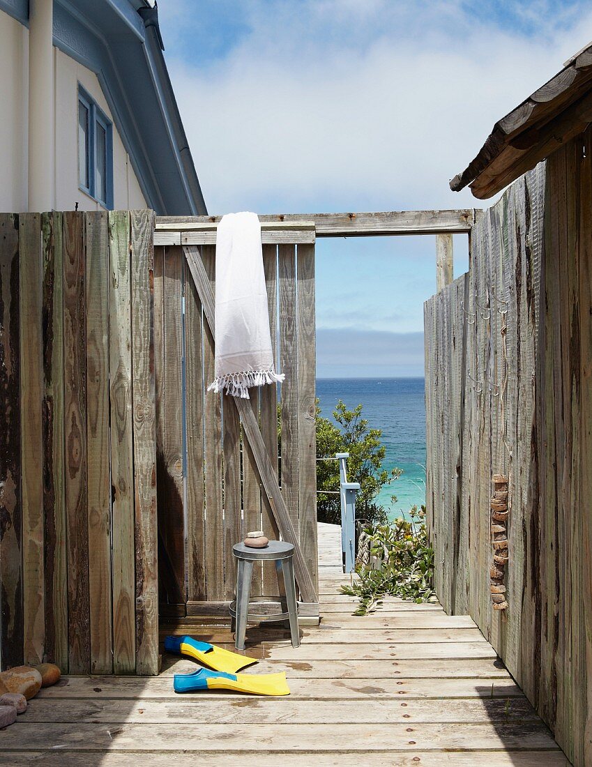 Flippers in weathered outdoor shower area; view of sea through open gate