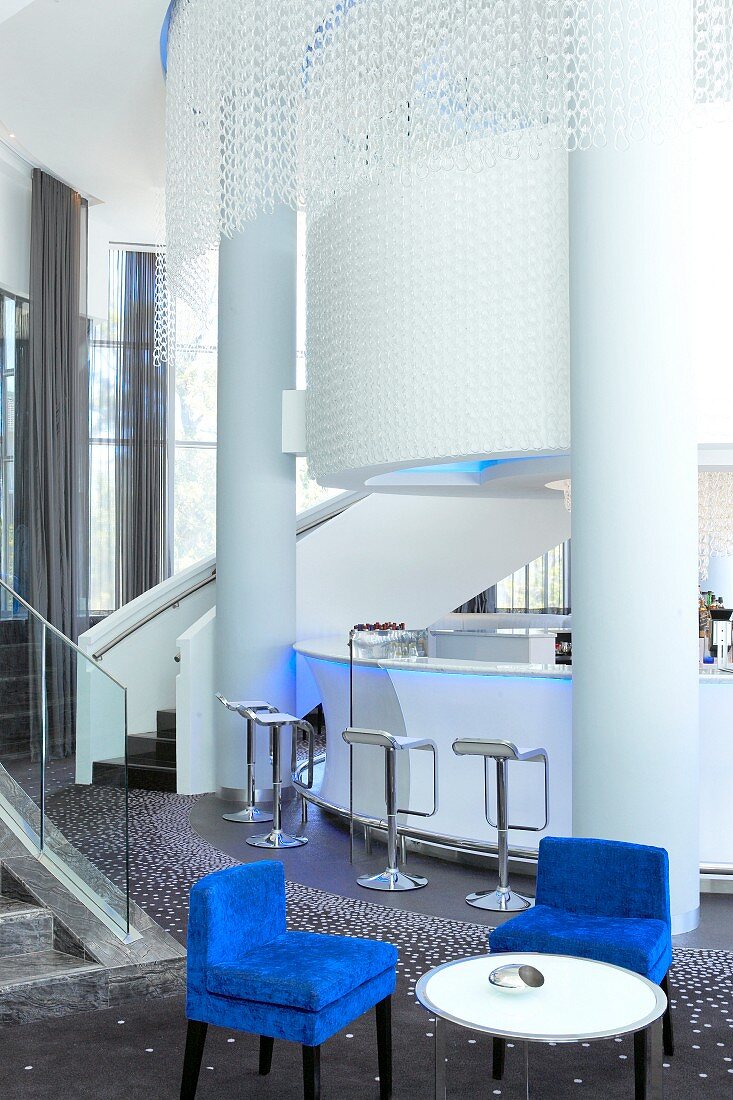 Tisch und blaue Stühle vor der Hotelbar mit weissen Säulen und Lichterketten neben dem Treppenaufgang ins Obergeschoss