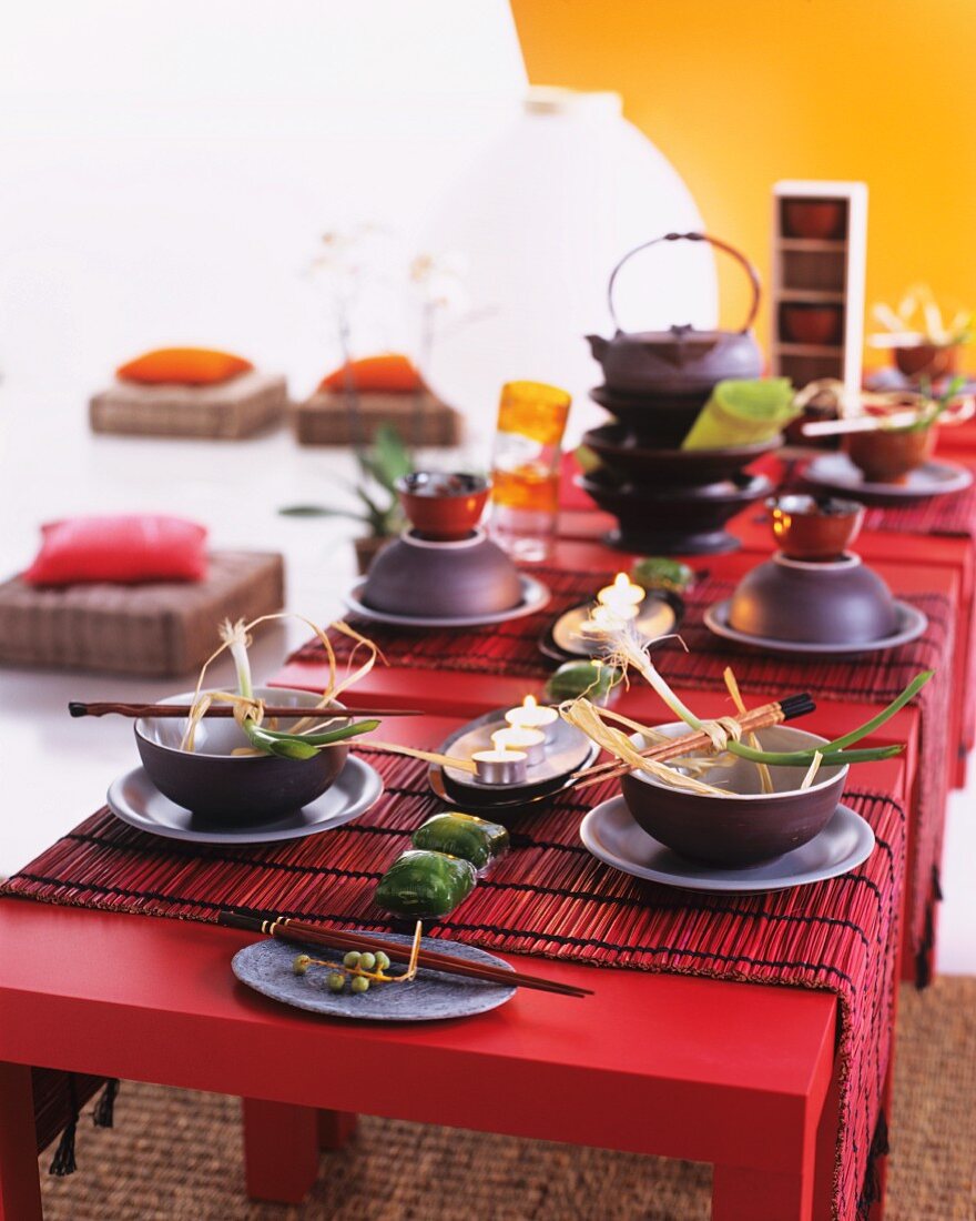 Asiatische Gedecke mit Blumendeko auf roten Tischen mit roten Bambusläufern