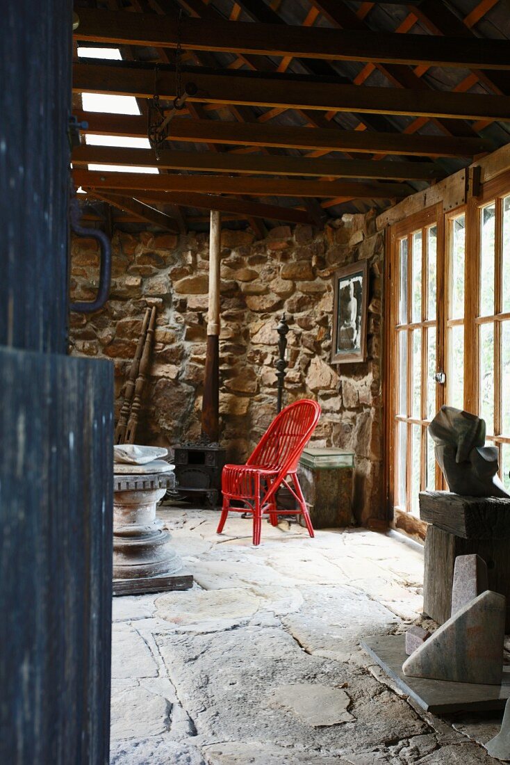 Rot lackierter Rattanstuhl auf Natursteinboden im Wohnraum eines Rustikos