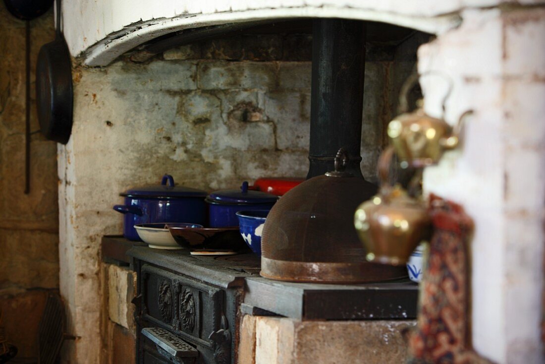 Blaue Emaille Kochtöpfe auf rustikalem Herd in schlichtem Landhaus